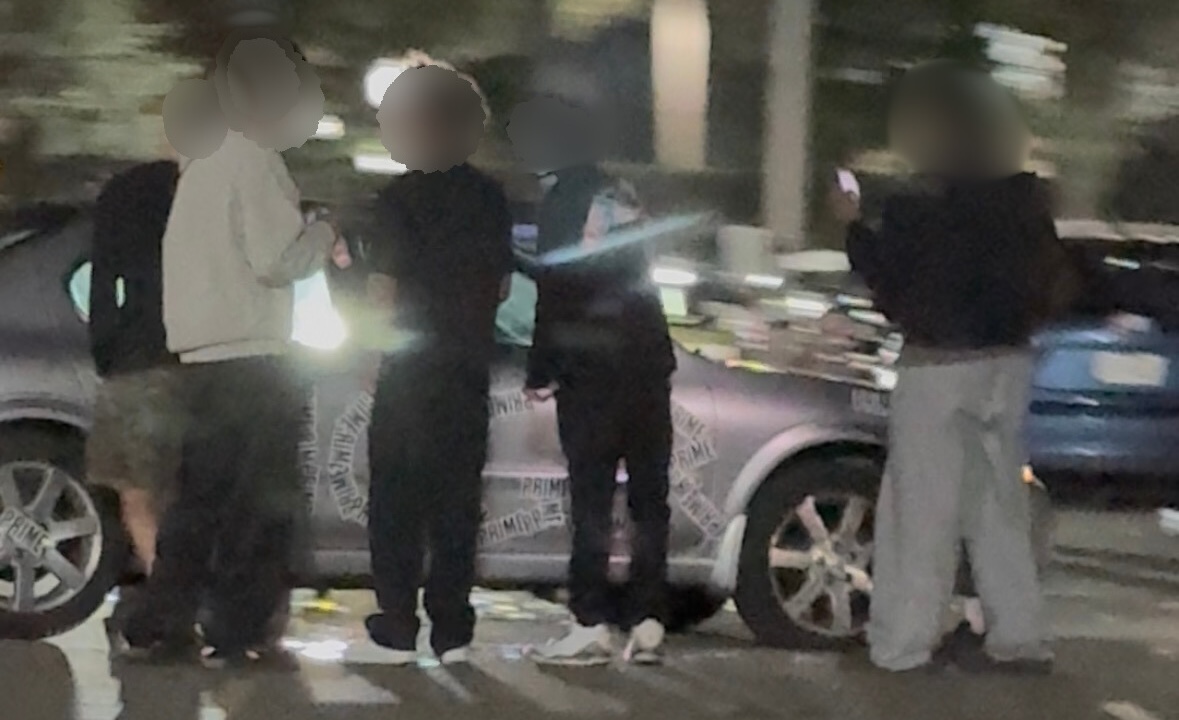Individuals surrounded the vandalized car. Some took photos while others pointed at the Prime stickers shaped into hate speech.